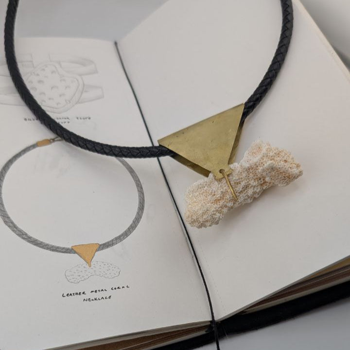 Necklace with gold triangle pendant and coral piece on an open traveler`s notebook.