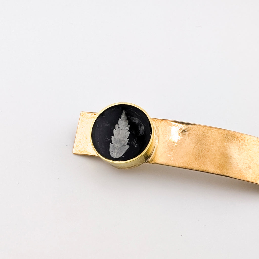 Gold hair clip with black and white fern on a light gray background
