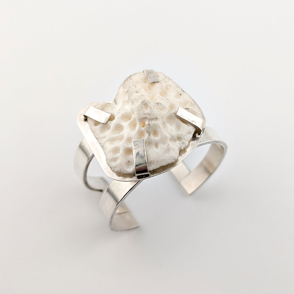 Silver arm cuff with bone set on top on a white background.