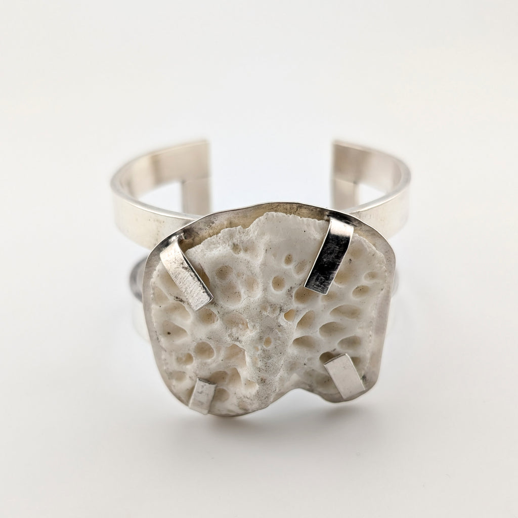 Silver arm cuff with bone set on top on a white background.