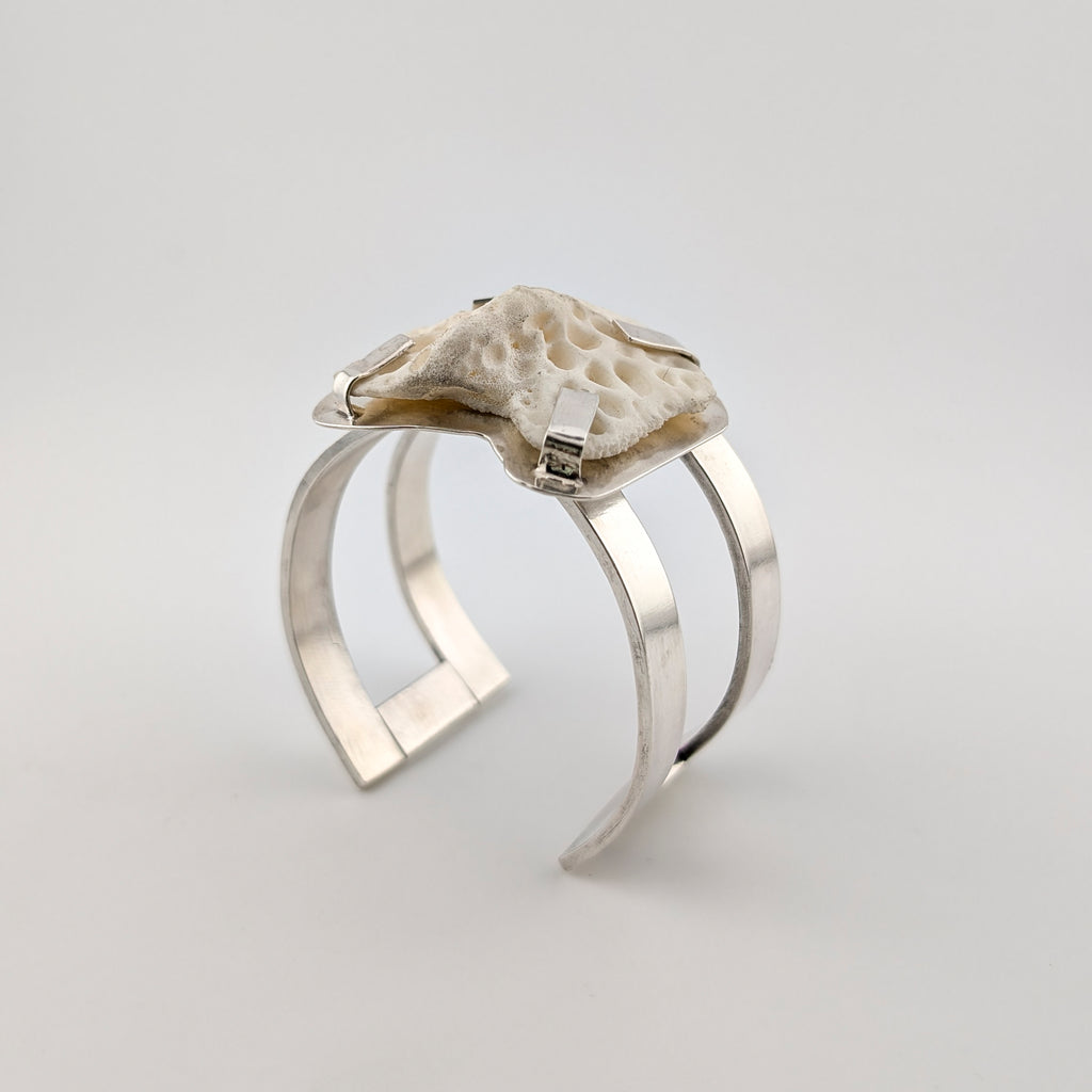 Silver arm cuff with bone set on top on a white background.