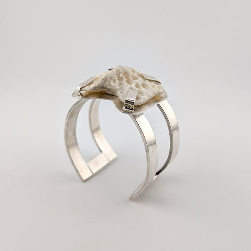 Silver arm cuff with bone set on top on a white background.