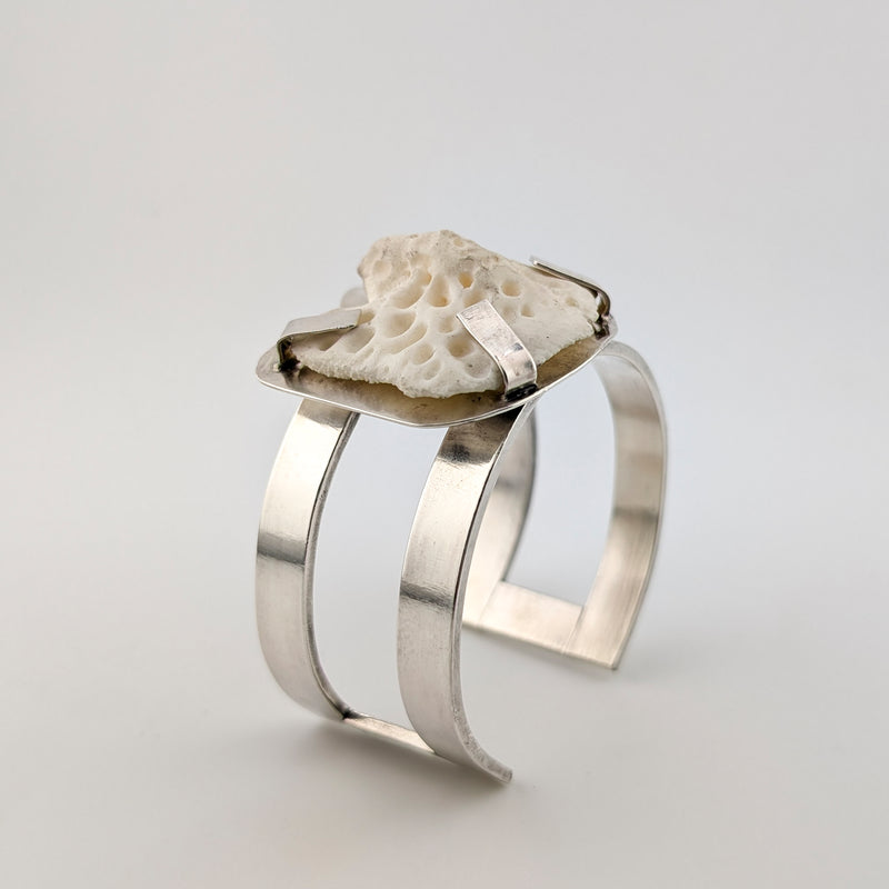 Silver arm cuff with bone set on top on a white background.