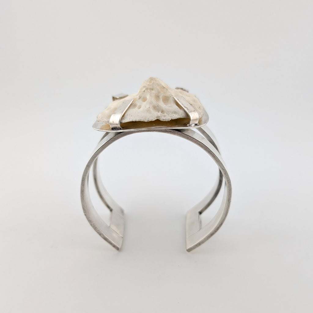 Silver arm cuff with bone set on top on a white background.