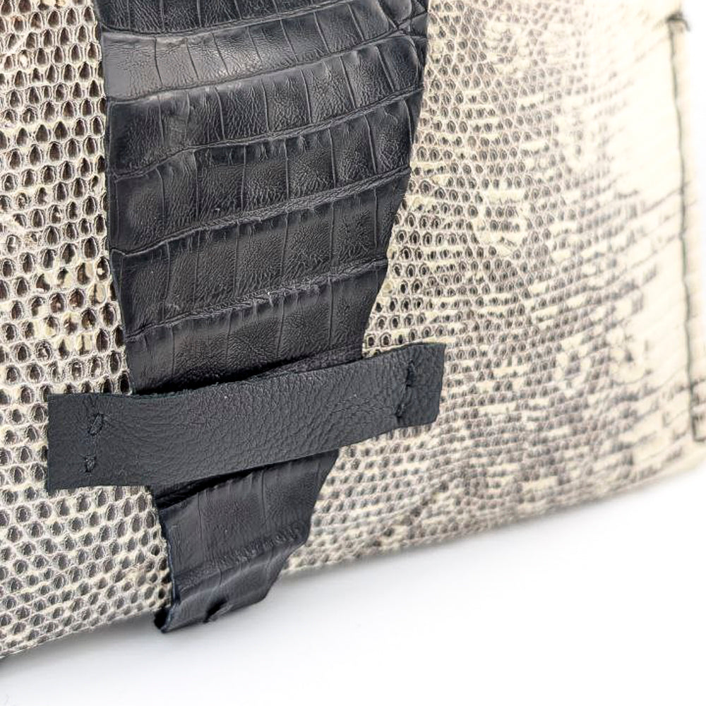 Close-up of a black and white lizard textured bag with black leather strap on a white background