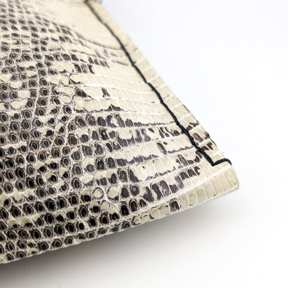 Close up detail shot of hand-sewn stitches on a black and white lizard leather clutch against a white background