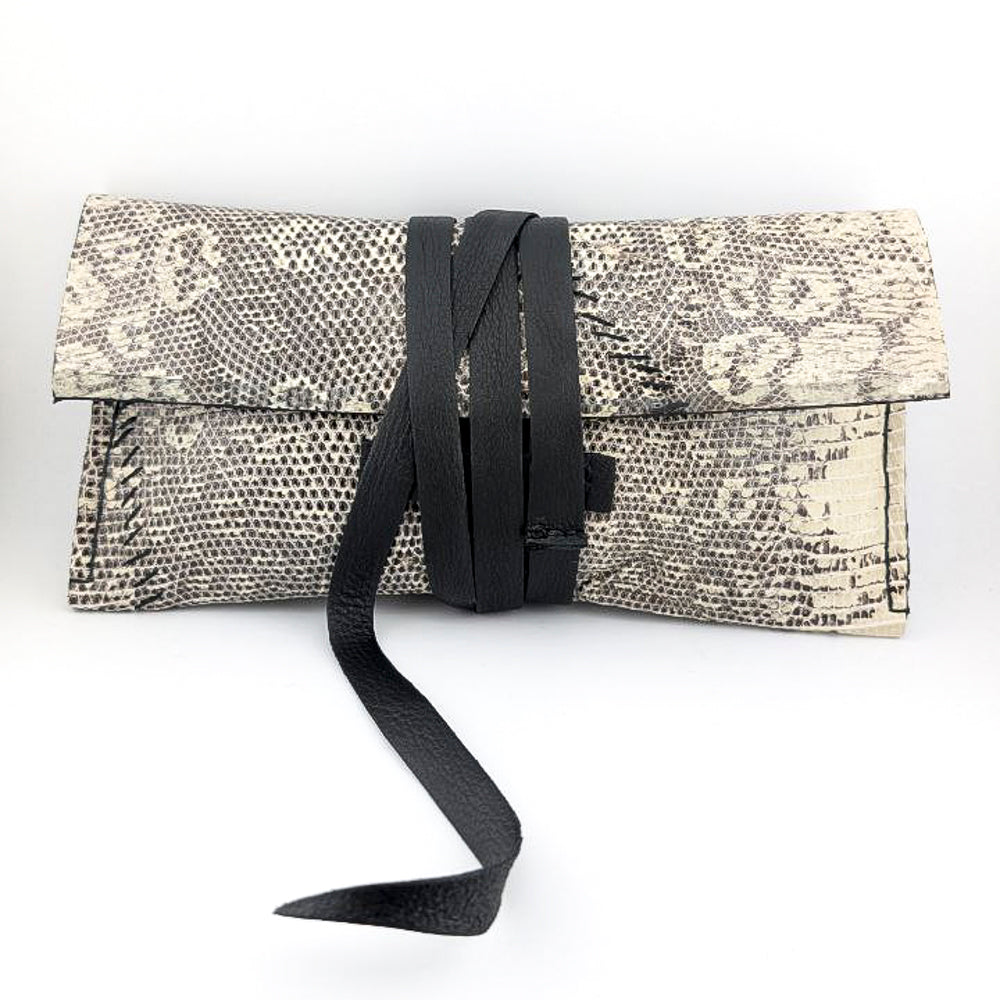 Clutch bag with black and white lizard skin leather and black strap on a white background