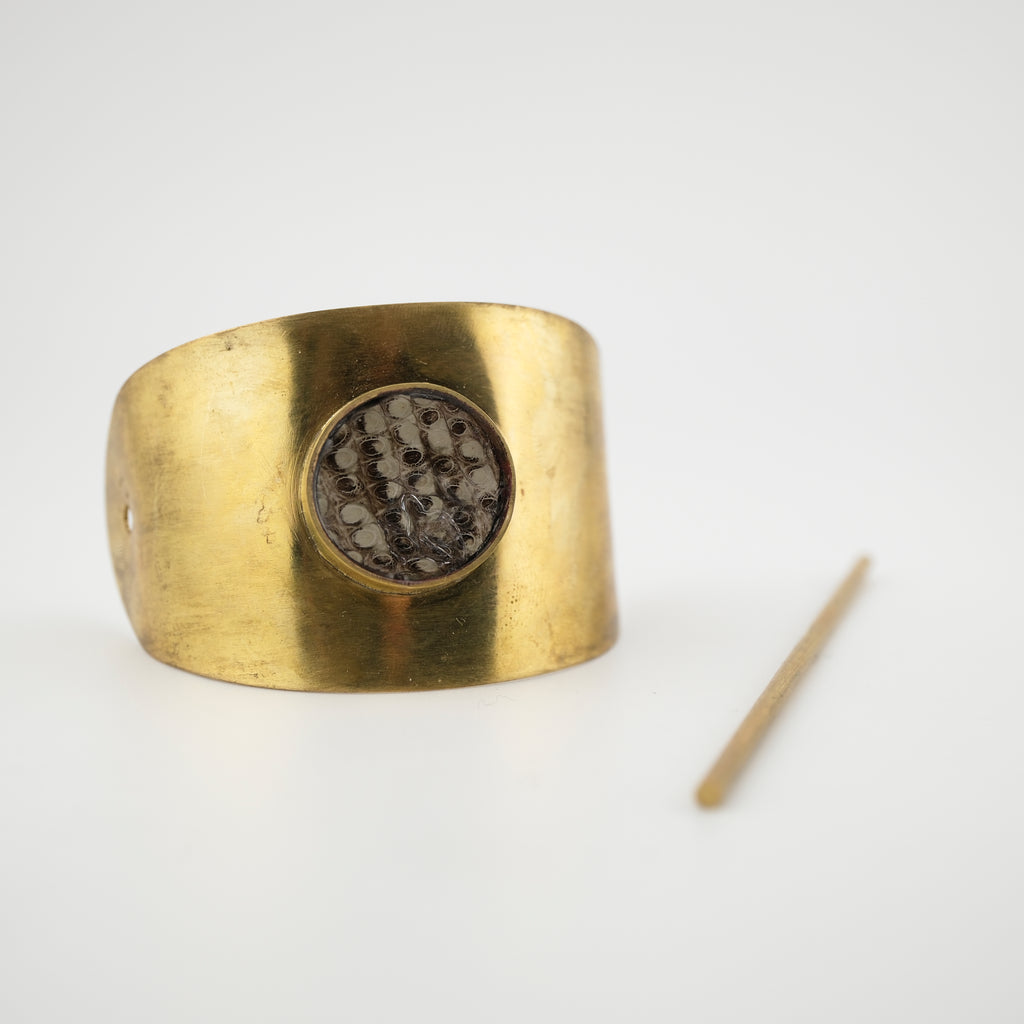 Gold cuff hair piece with a central setting of lizard skin on a white background.
