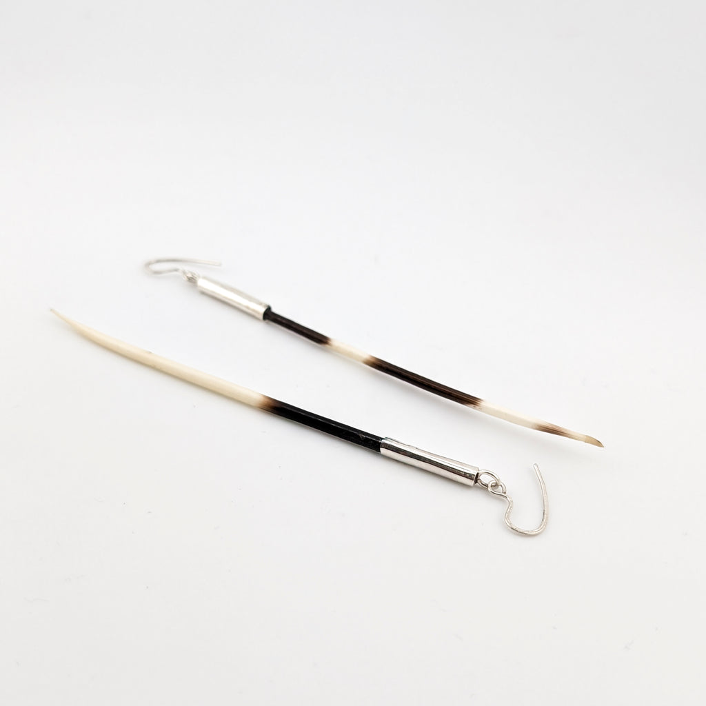 Two brown and white porcupine earrings set in silver cuffs against a white background.