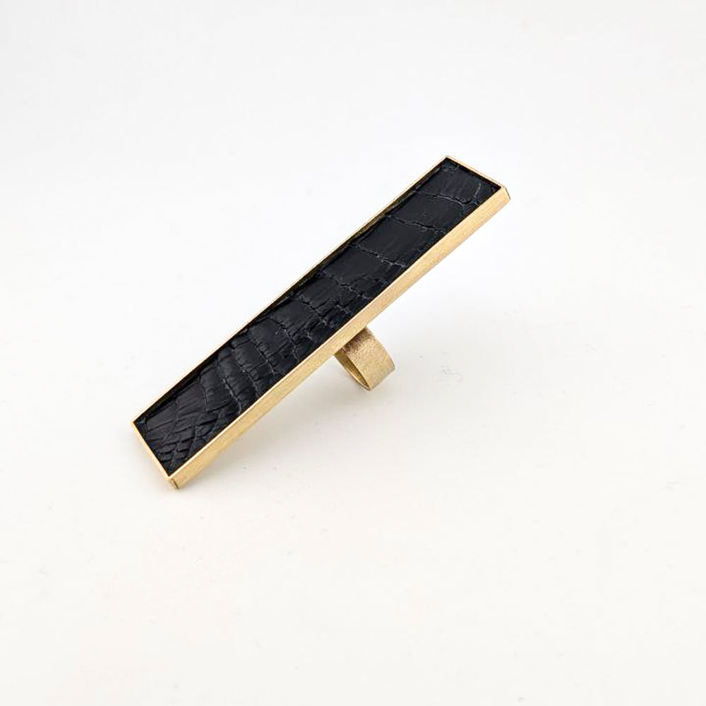 Brass rectangular ring with black caiman leather embedded inside against a white background.