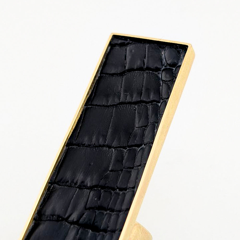 Brass rectangular ring with black caiman leather embedded inside against a white background.