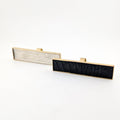 Two brass rectangular rings with black caiman leather  and white cowhide embedded inside against a white background.