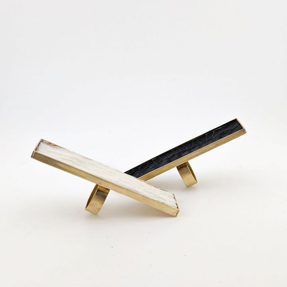 Two brass rectangular rings with black caiman leather  and white cowhide embedded inside against a white background.