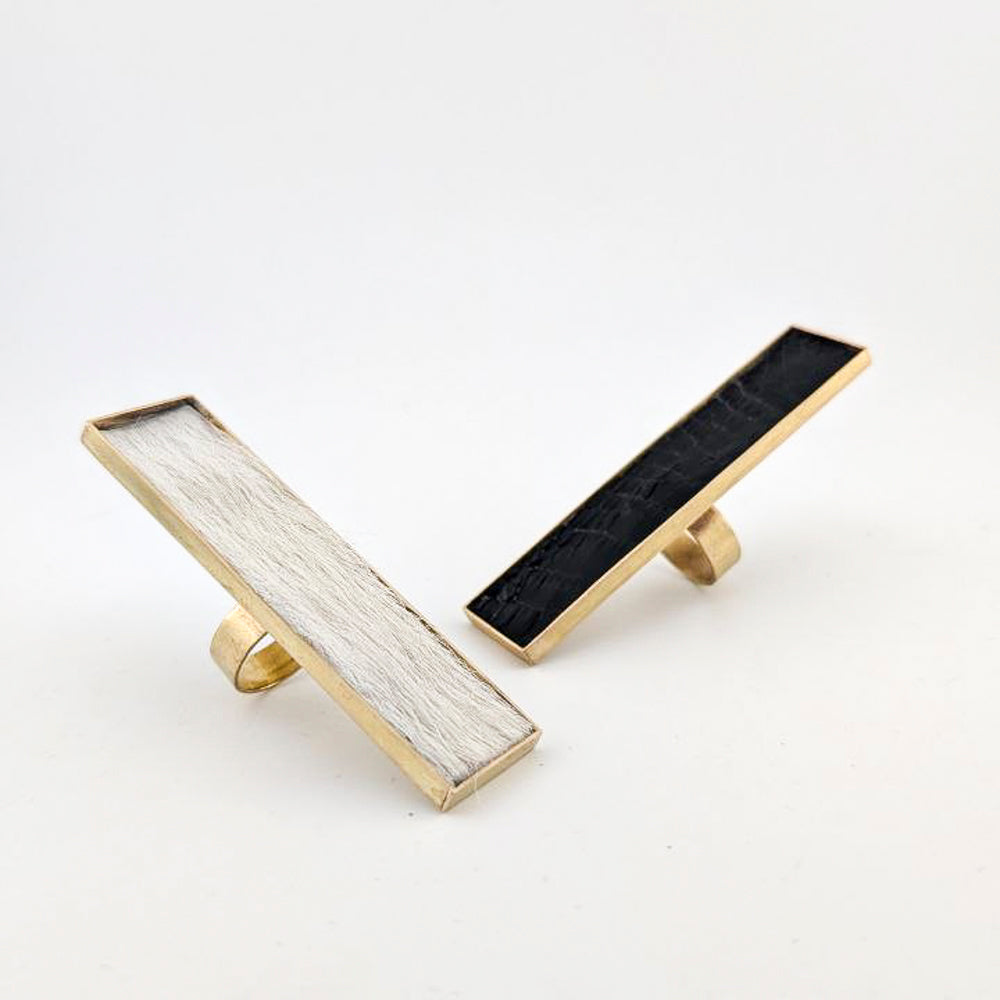Two brass rectangular rings with black caiman leather  and white cowhide embedded inside against a white background.