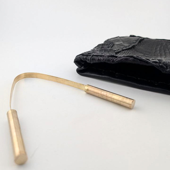 Brass tongue scraper with black leather pouch on white background