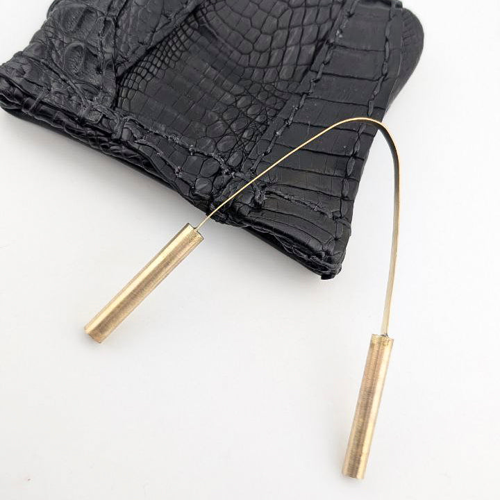 Brass tongue scraper with black leather pouch on white background