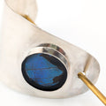 Silver hair piece with a blue and black butterfly wing inlay and brass accents on a white background