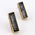 Pair of rectangular earrings with black and gold design on a white background