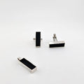 Pair of silver cufflinks  and silver rectangular pendant with black rectangular slots on a white background